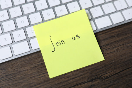 Paper note with phrase Join Us and keyboard on wooden table, closeupの写真素材