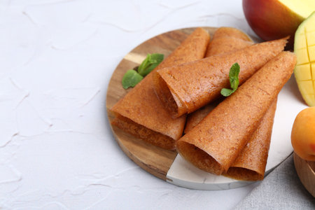 Delicious fruit leather rolls, mint and mango on white table, closeup. Space for textの写真素材