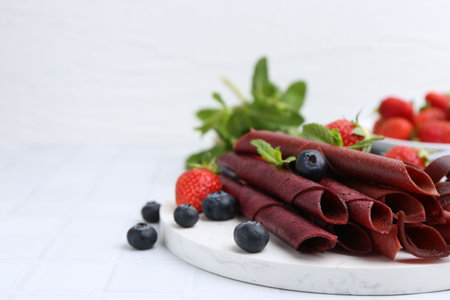Tasty fruit leather rolls, strawberries, blueberries and mint on white tiled table, closeup. Space for textの写真素材