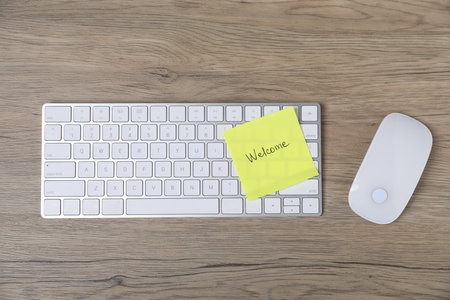 Sticky note with word Welcome, computer keyboard and mouse on wooden table, flat layの写真素材