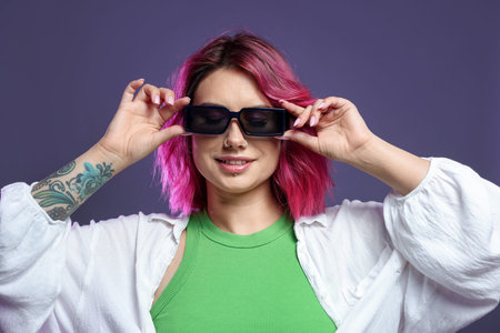 Beautiful woman with pink dyed hair in sunglasses on violet background