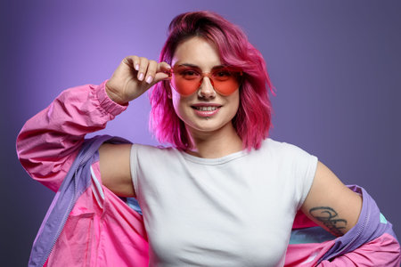 Beautiful woman with pink dyed hair in sunglasses on violet gradient background