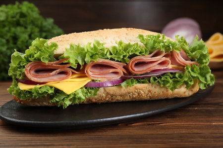 Tasty baguette sandwich with ham, cheese and vegetables on wooden table against dark background, closeupの写真素材