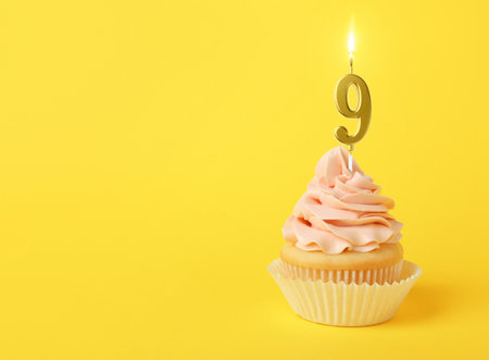 Yummy cupcake with burning golden candle in shape of number 9 on yellow background, space for text. Birthday or other special occasionの写真素材
