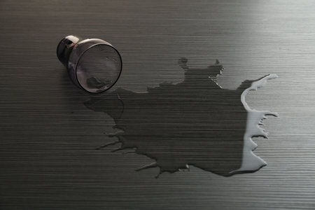 Overturned glass and spilled water on wooden tableの写真素材