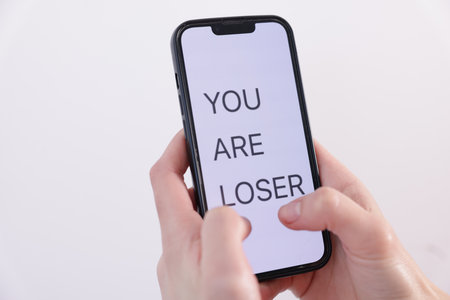 Cyber bullying. Woman holding smartphone with text You Are Loser on white background, closeupの写真素材