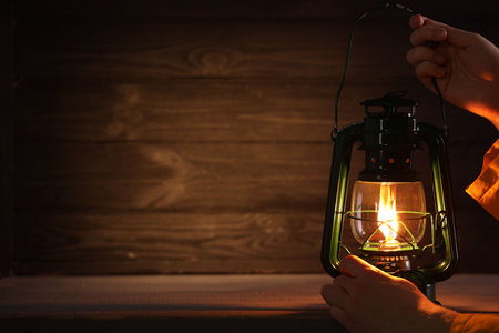 Man with vintage kerosene lamp on wooden background, closeup. Space for textの写真素材