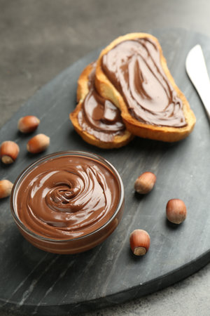 Tasty chocolate spread, toasts and hazelnuts on gray table, closeupの写真素材