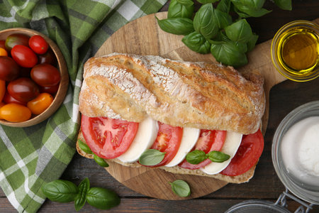 Tasty sandwich with mozzarella cheese, tomatoes and basil on wooden table, flat layの写真素材
