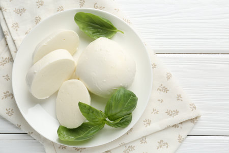 Pieces of delicious mozzarella cheese and basil on white wooden table, top viewの写真素材