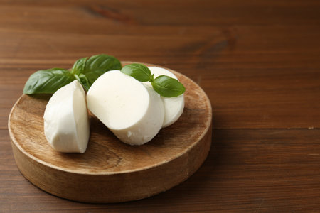 Pieces of delicious mozzarella cheese and basil leaves on wooden table, closeup. Space for textの写真素材