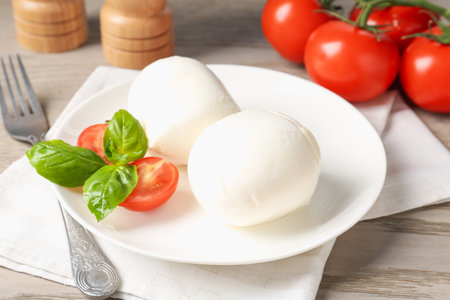 Tasty mozzarella cheese balls, tomatoes and basil on wooden table, closeupの写真素材