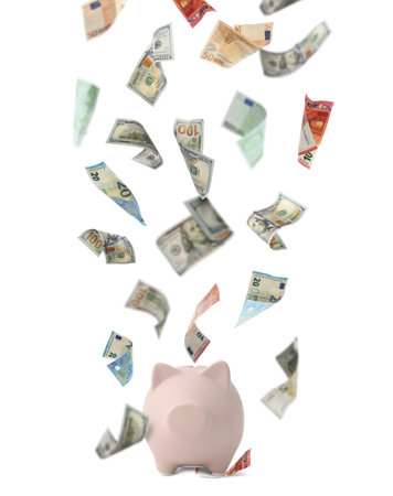 Different banknotes falling into piggy bank on white backgroundの写真素材