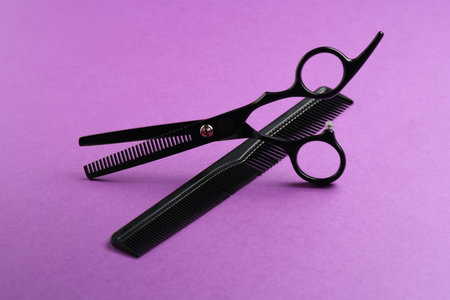 Scissors and comb on violet background, closeup. Hairdresser's tools