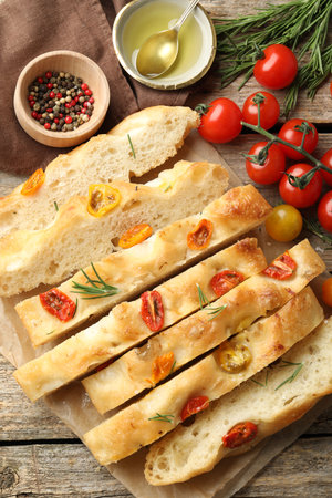 Cut delicious focaccia with tomatoes, spices and oil on wooden table, flat layの写真素材