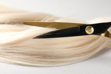 Cutting blonde hair lock with scissors on light grey background, closeupの写真素材