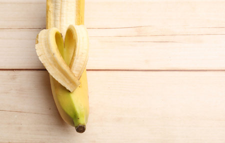 Banana with heart made of peel on wooden table, top view. Space for textの写真素材