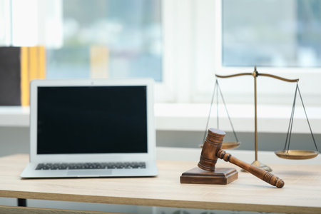 Laptop, judge's gavel and scales on wooden table in office