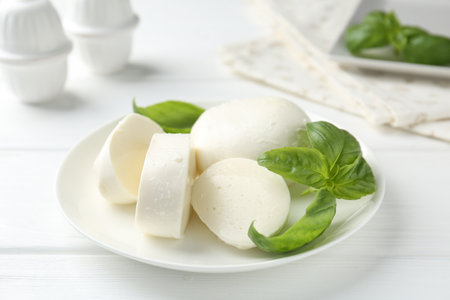 Pieces of delicious mozzarella cheese and basil on white wooden table, closeupの写真素材
