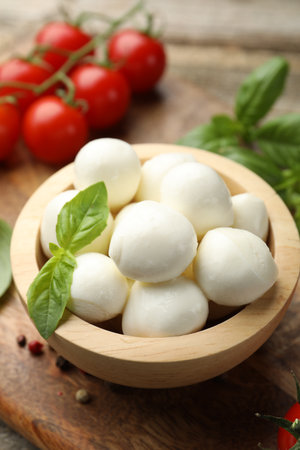 Tasty mozzarella cheese balls in bowl, basil, peppercorns and tomatoes on table, closeupの写真素材