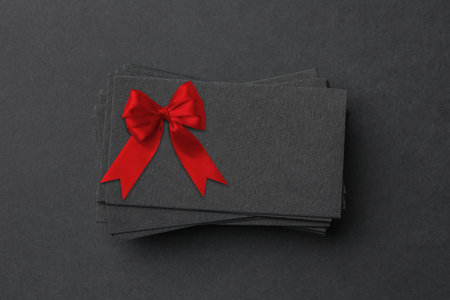 Blank gift card with red bow on black background, above view. Mockup for designの写真素材