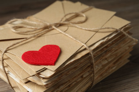 Stack of love letters and paper heart on wooden table, closeup