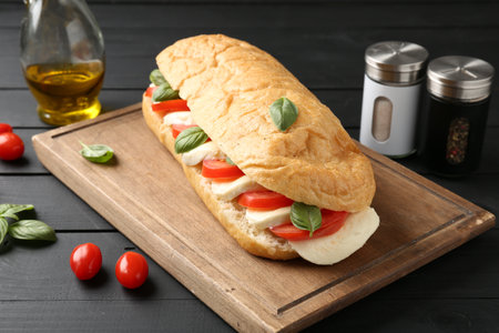 Tasty sandwich with mozzarella cheese, tomatoes and basil on black wooden table, closeupの写真素材