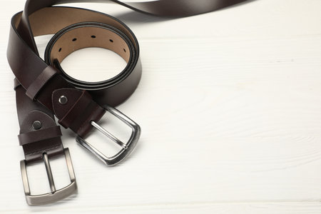 Two brown leather belts on white wooden table, above view. Space for textの写真素材