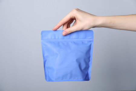Woman with zipper stand-up pouch on grey background, closeup. Mockup for design