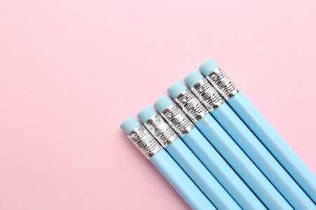 Graphite pencils with erasers on pink background, flat lay. Space for text