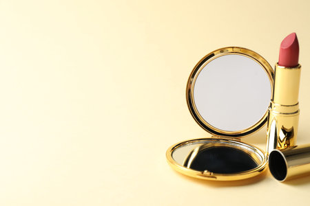 Open pocket mirror and lipstick on beige background, closeup. Space for textの写真素材