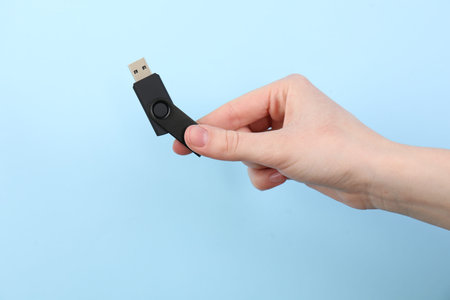 Woman holding USB flash drive on light blue background, closeupの写真素材