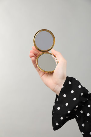 Woman holding open pocket mirror on grey background, closeupの写真素材