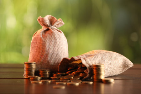 Burlap bags and stacked coins on wooden table against blurred backgroundの写真素材