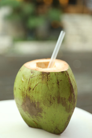 Green coconut with refreshing drink and straw on white table outdoors, closeupの写真素材
