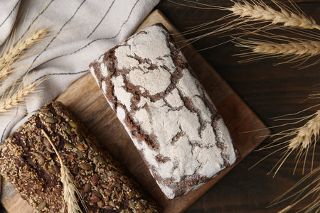 Freshly baked loaves of bread and spikes on wooden table, flat lay