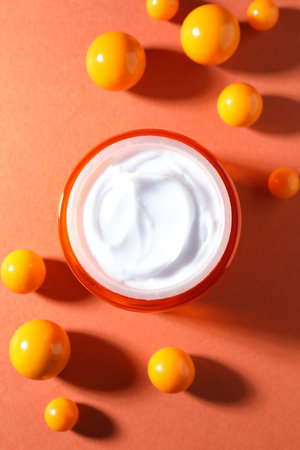 Jar of moisturizing body cream and balls on orange background, flat lay