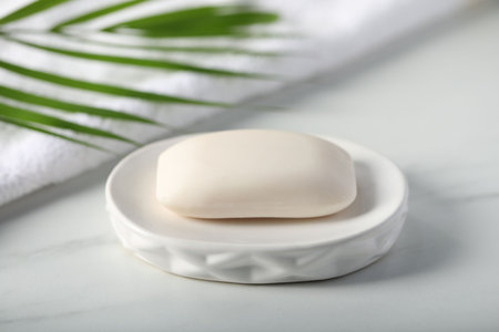Soap bar, towel and palm leaf on white marble table, closeup