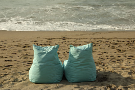 Turquoise bean bag chairs on sandy beach by seaの写真素材