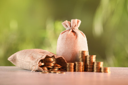 Burlap bags and stacked coins on table against blurred backgroundの写真素材