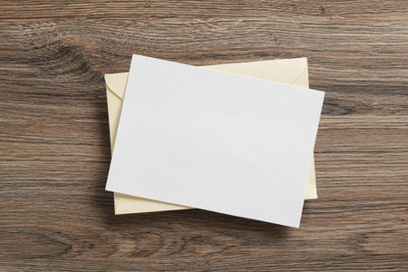 Blank invitation card and envelope on wooden table, top view. Space for design
