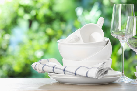 Different clean dishes on wooden table against blurred green background, space for text