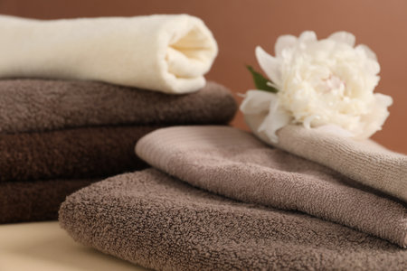 Soft towels and peony flower on beige table against brown background, closeupの写真素材