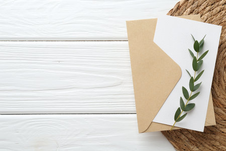 Blank invitation card, envelope, branch and wicker mat on white wooden table, top view. Space for textの写真素材