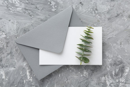Blank invitation card, branch and envelope on grey textured table, top view