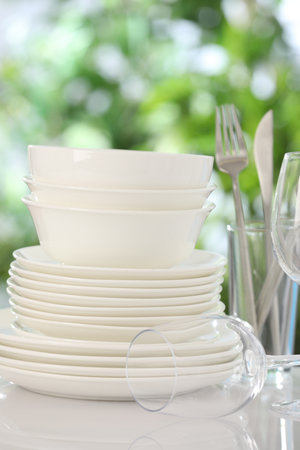 Different clean dishes on white table against blurred green background, closeupの写真素材