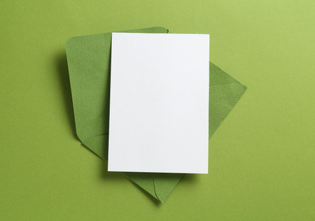 Blank invitation card and envelope on green background, top view. Space for designの写真素材