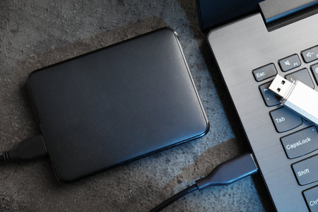 USB flash drive, hard disk drive with cable and laptop on dark grey table, flat layの写真素材