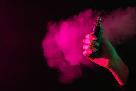 Woman using electronic smoking device in neon lights on black background, closeup. Space for textの写真素材