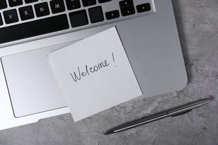 Sticky note with word Welcome, pen and laptop on grey table, flat layの写真素材
